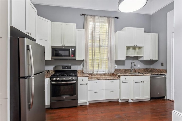 kitchen with dark stone countertops, white cabinets, stainless steel appliances, and a sink