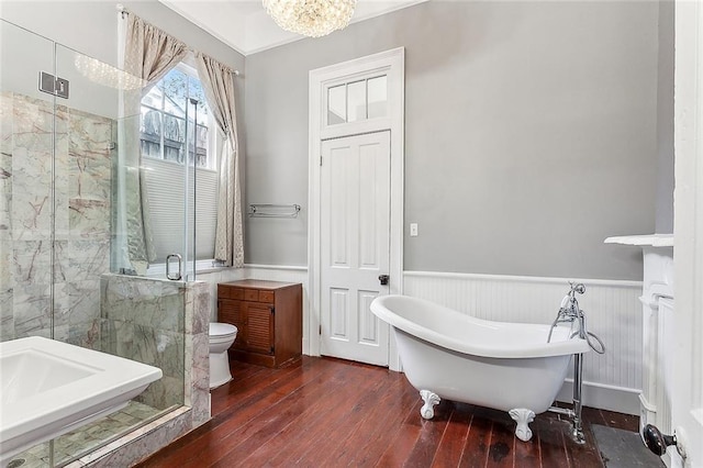 bathroom with a freestanding tub, a shower stall, wood-type flooring, wainscoting, and a notable chandelier