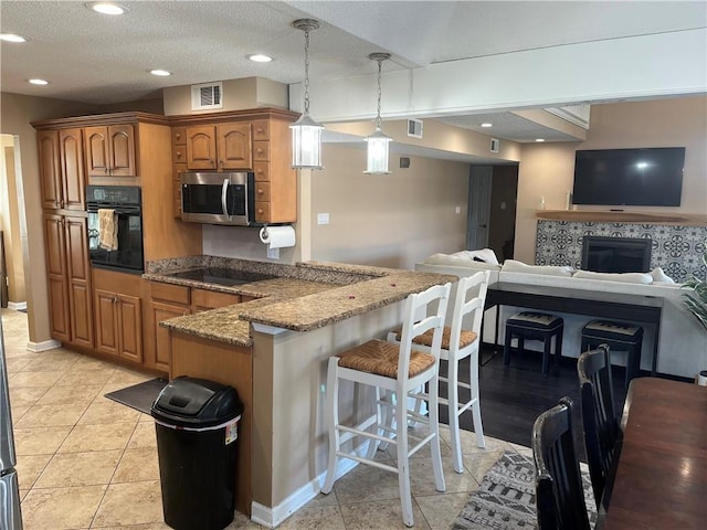 kitchen featuring a breakfast bar, black appliances, light tile patterned floors, dark stone countertops, and hanging light fixtures