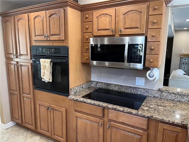 kitchen with dark stone counters, light tile patterned floors, black appliances, and a textured ceiling