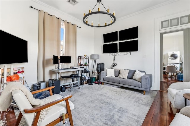 living room with dark hardwood / wood-style floors, ornamental molding, stacked washer and dryer, and an inviting chandelier