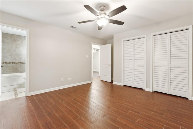 unfurnished bedroom featuring ceiling fan, two closets, and ensuite bath