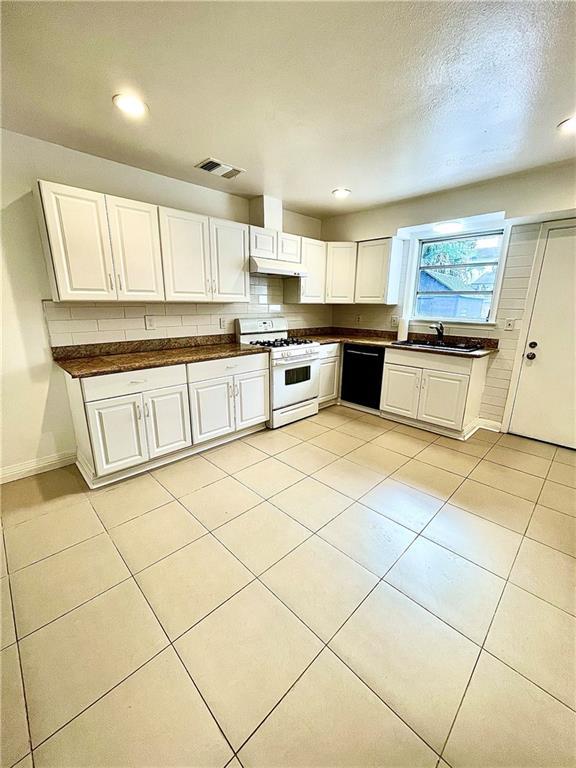 kitchen featuring dishwasher, white cabinets, sink, light tile patterned floors, and gas range gas stove