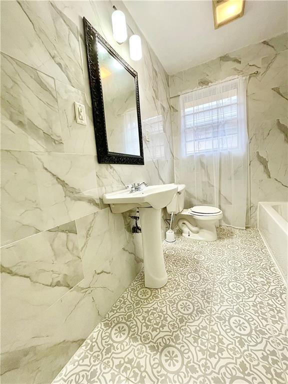 bathroom with toilet, a tub, and tile walls