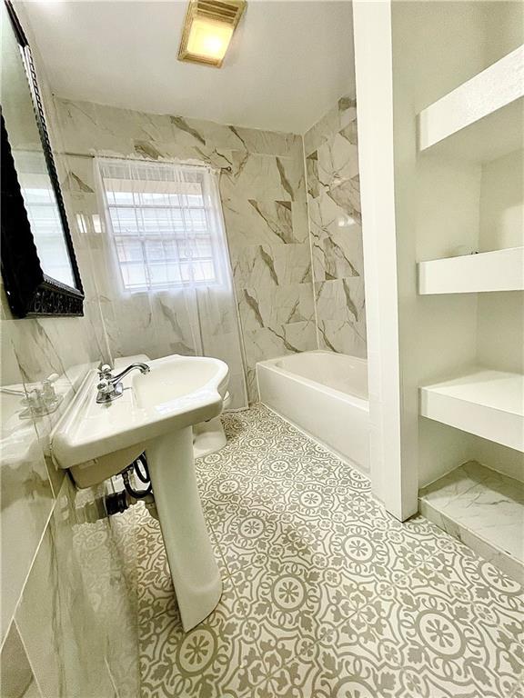 bathroom with tile patterned flooring, toilet, tiled shower / bath, and tile walls