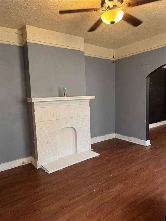 unfurnished living room with ceiling fan, dark hardwood / wood-style floors, a brick fireplace, and a textured ceiling