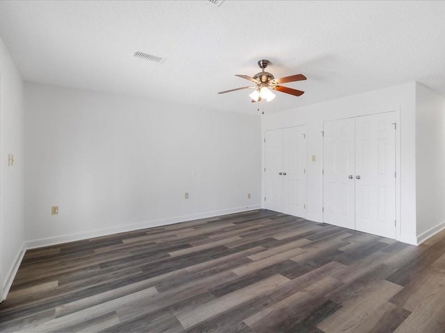 unfurnished bedroom featuring a textured ceiling, ceiling fan, dark hardwood / wood-style flooring, and two closets