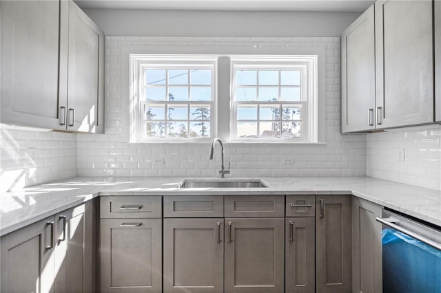 kitchen with backsplash, dishwasher, sink, and light stone counters