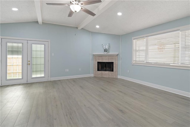 unfurnished living room featuring vaulted ceiling with beams, french doors, light hardwood / wood-style floors, and a tiled fireplace