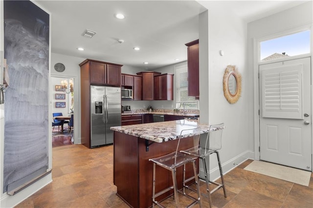 kitchen with stainless steel appliances, light stone countertops, a kitchen breakfast bar, and kitchen peninsula