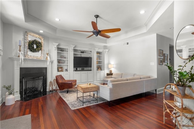 living room with built in shelves, ornamental molding, dark hardwood / wood-style floors, a tray ceiling, and ceiling fan