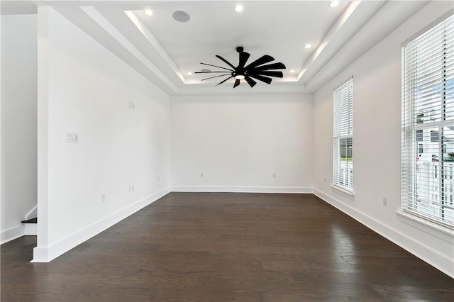 empty room featuring a raised ceiling, ceiling fan, and dark hardwood / wood-style flooring