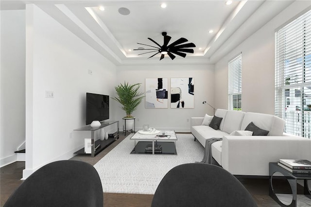 living room featuring a tray ceiling, ceiling fan, and dark wood-type flooring