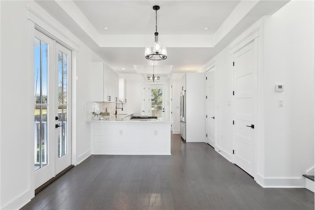 kitchen featuring tasteful backsplash, kitchen peninsula, pendant lighting, a tray ceiling, and white cabinets