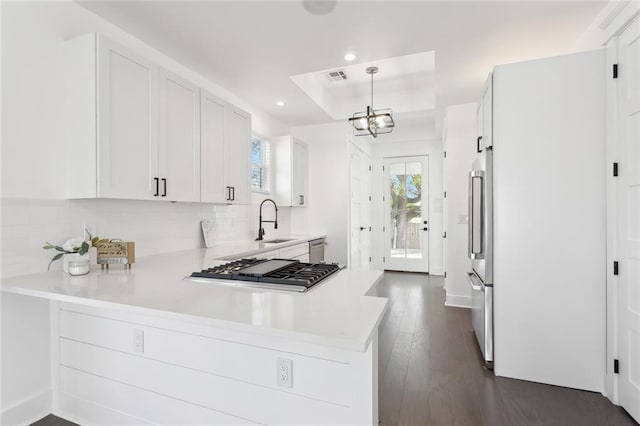 kitchen featuring a tray ceiling, stainless steel appliances, sink, pendant lighting, and white cabinetry