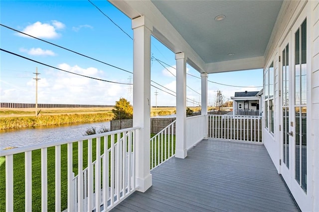 wooden terrace with a lawn, a water view, and a porch