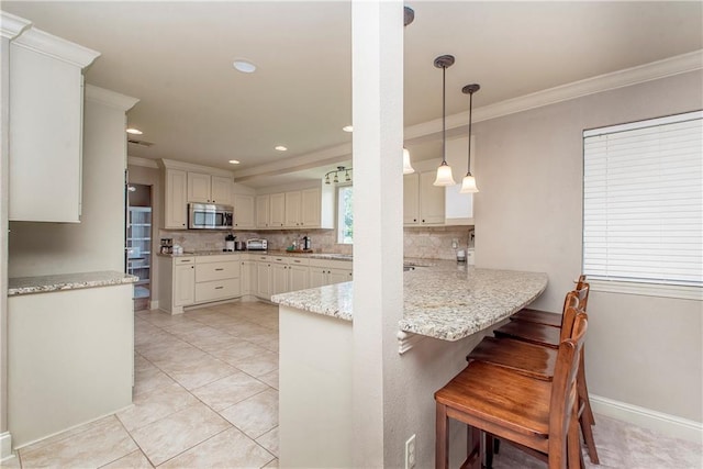 kitchen featuring a breakfast bar, a peninsula, ornamental molding, stainless steel microwave, and tasteful backsplash