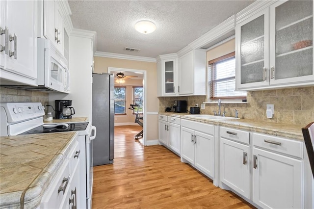 kitchen with white appliances, white cabinets, ceiling fan, ornamental molding, and a textured ceiling