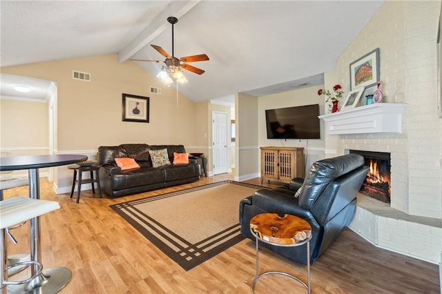 living room featuring lofted ceiling with beams, a brick fireplace, ceiling fan, light wood-type flooring, and ornamental molding