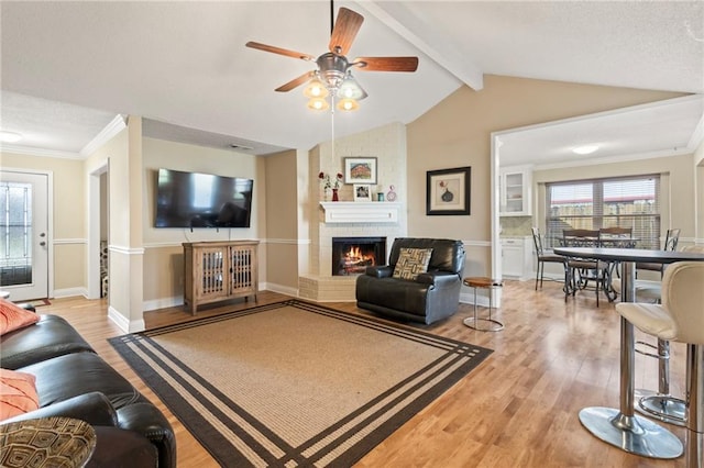 living room featuring ceiling fan, vaulted ceiling with beams, light hardwood / wood-style floors, a fireplace, and ornamental molding