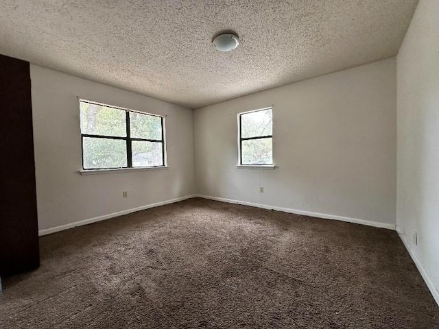 spare room featuring dark carpet and a textured ceiling