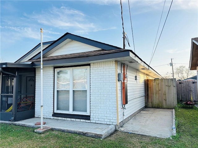 view of property exterior featuring fence, brick siding, and a sunroom