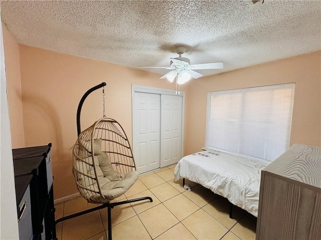 bedroom featuring a closet, light tile patterned floors, a textured ceiling, and a ceiling fan