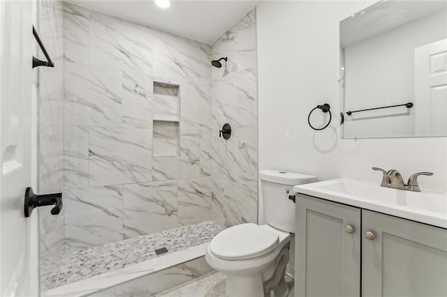 bathroom with a tile shower, vanity, and toilet