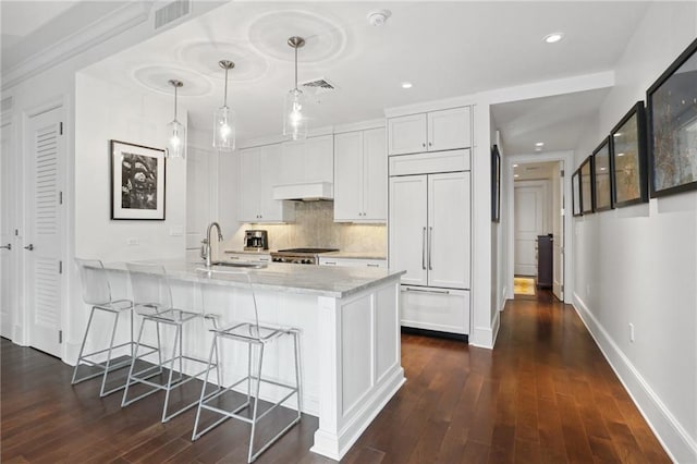 kitchen with paneled refrigerator, light stone counters, sink, decorative light fixtures, and white cabinets