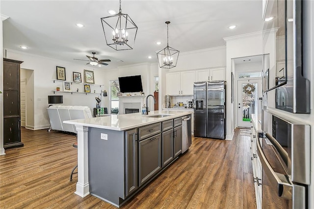 kitchen featuring crown molding, stainless steel appliances, light countertops, open floor plan, and a sink