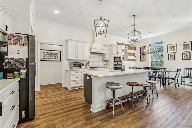 kitchen with a breakfast bar area, premium range hood, a sink, appliances with stainless steel finishes, and ornamental molding