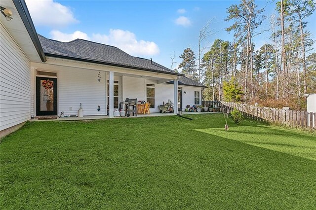 rear view of house with a patio area, a shingled roof, fence, and a yard