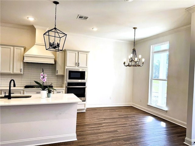 kitchen featuring visible vents, appliances with stainless steel finishes, an inviting chandelier, premium range hood, and a sink