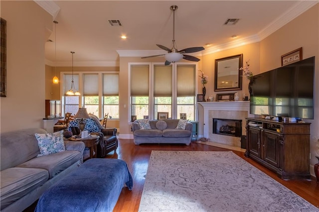 living room featuring dark hardwood / wood-style flooring, ceiling fan, crown molding, and a tiled fireplace