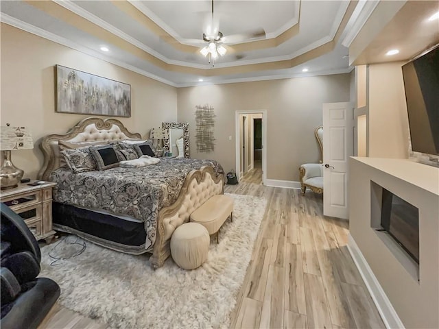 bedroom featuring ceiling fan, light wood-type flooring, ornamental molding, and a tray ceiling