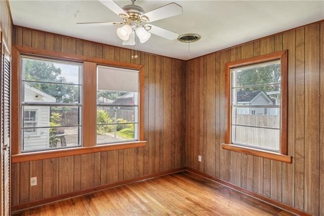 spare room featuring wood walls, light wood-type flooring, and a wealth of natural light