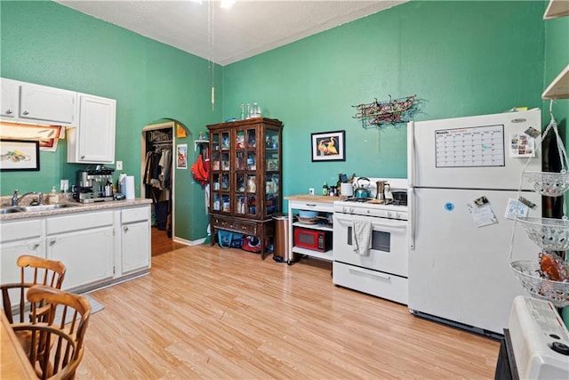 kitchen featuring white cabinetry, sink, white appliances, and light hardwood / wood-style flooring