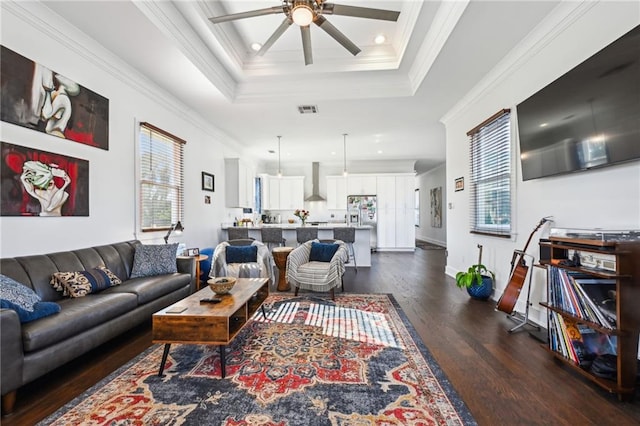 living room featuring a raised ceiling, ceiling fan, crown molding, and dark wood-type flooring