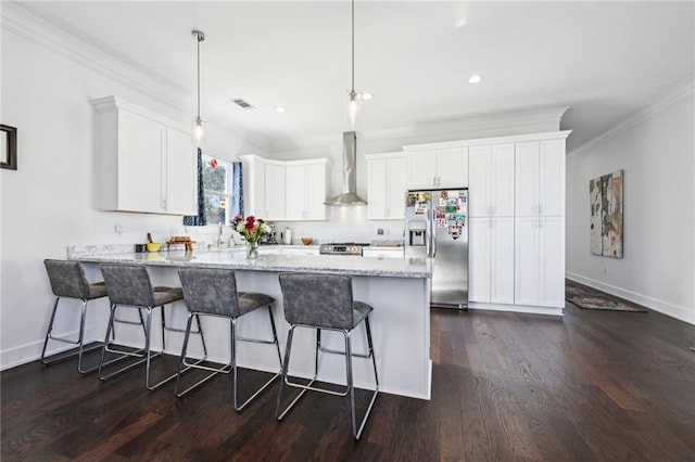 kitchen with stainless steel refrigerator with ice dispenser, a kitchen breakfast bar, wall chimney exhaust hood, decorative light fixtures, and white cabinetry