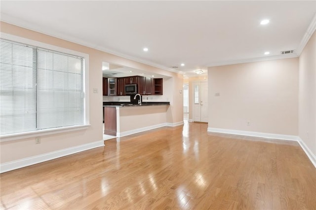 unfurnished living room with light wood-type flooring, crown molding, and sink