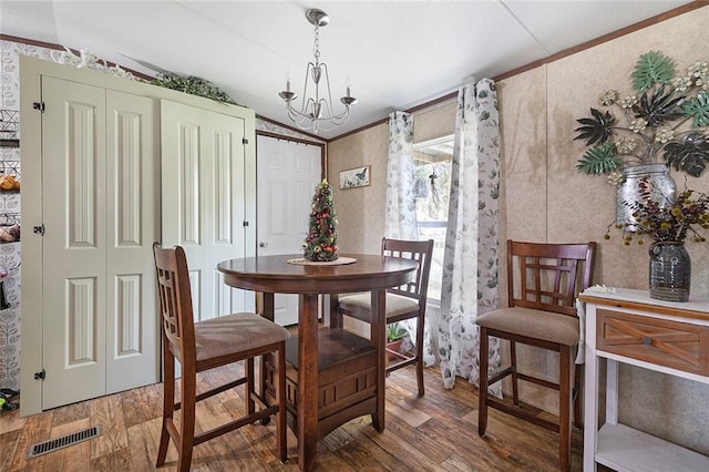 dining space featuring vaulted ceiling, wood-type flooring, ornamental molding, and an inviting chandelier