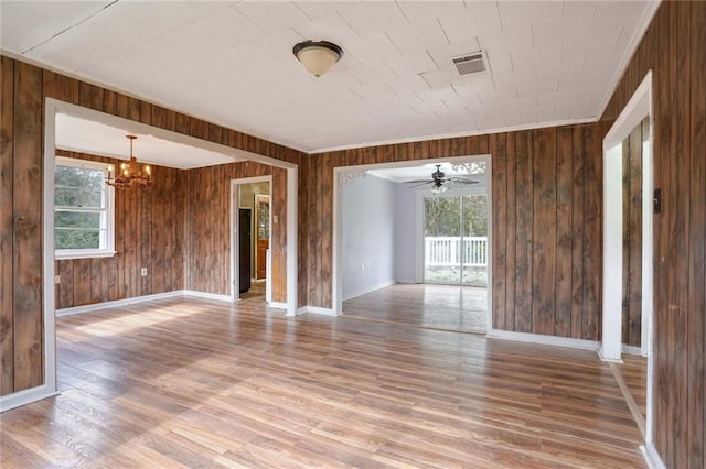 interior space with ceiling fan with notable chandelier, hardwood / wood-style flooring, and wood walls