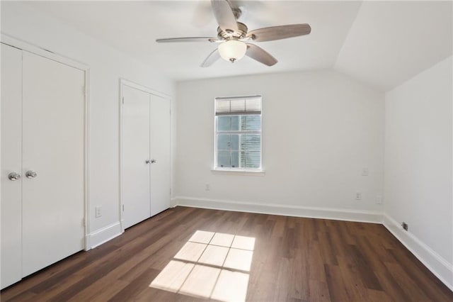 unfurnished bedroom featuring ceiling fan, dark hardwood / wood-style floors, multiple closets, and vaulted ceiling