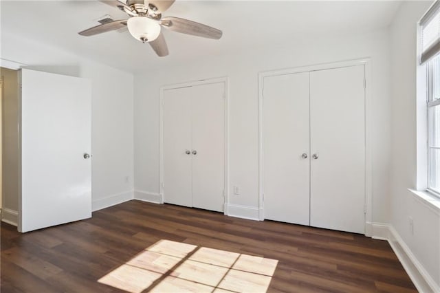 unfurnished bedroom with ceiling fan, dark hardwood / wood-style flooring, and two closets