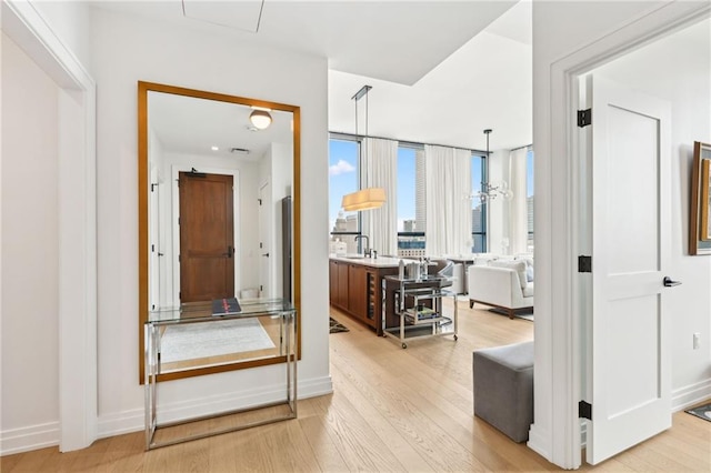 hall with light hardwood / wood-style floors, an inviting chandelier, and sink