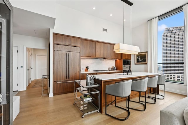 kitchen featuring a center island with sink, sink, hanging light fixtures, paneled fridge, and light hardwood / wood-style floors