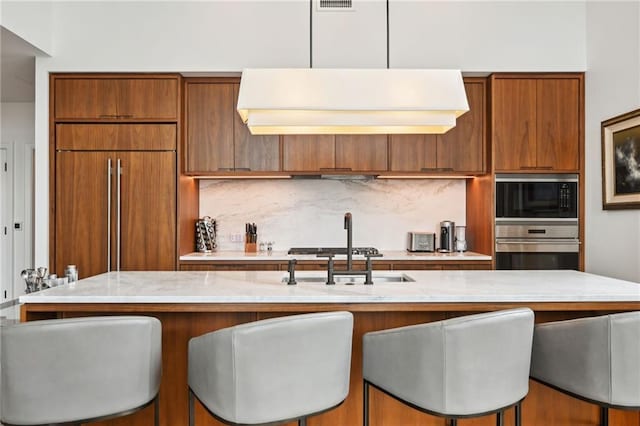 kitchen with built in appliances, tasteful backsplash, hanging light fixtures, and a breakfast bar area