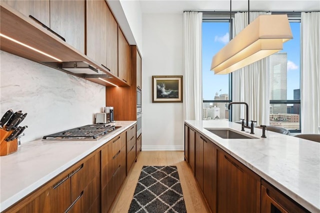 kitchen with sink, stainless steel gas cooktop, tasteful backsplash, light hardwood / wood-style floors, and pendant lighting