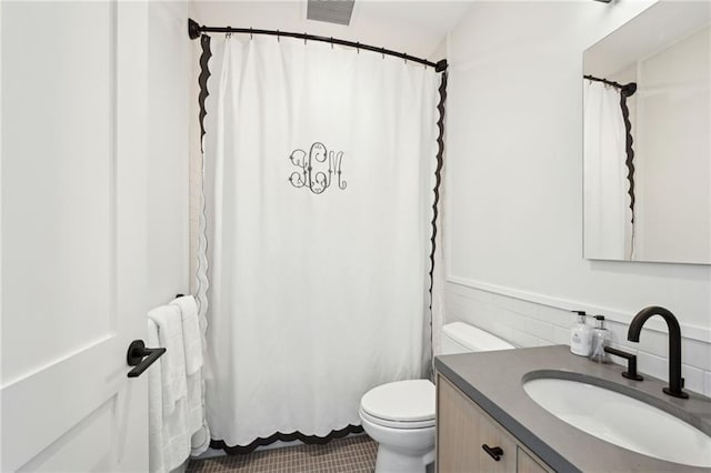 bathroom featuring vanity, toilet, and tile walls