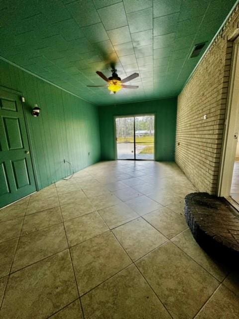 empty room featuring ceiling fan and brick wall